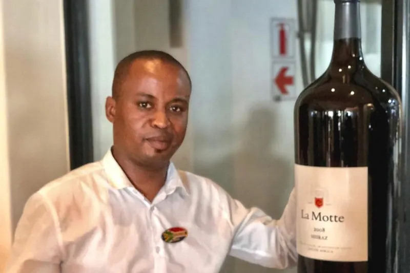 A JAP team member smiling beside a large bottle of wine at a wine estate