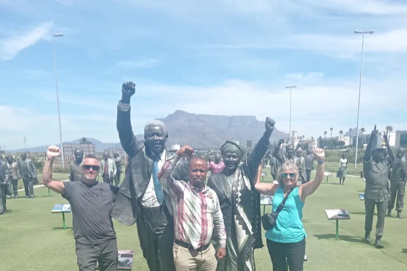 Guests raising their fists beside the bronze Long March to Freedom statues, Table Mountain behind